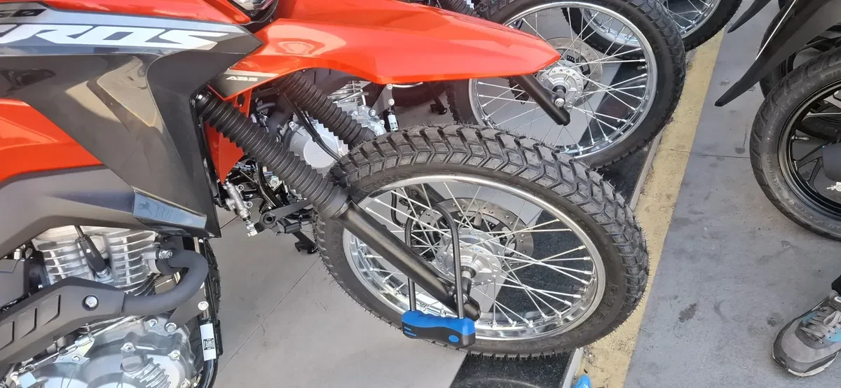 Cadeado em U azul travando a roda dianteira de uma moto de trilha laranja, um dos acessórios para scooter elétrica de segurança