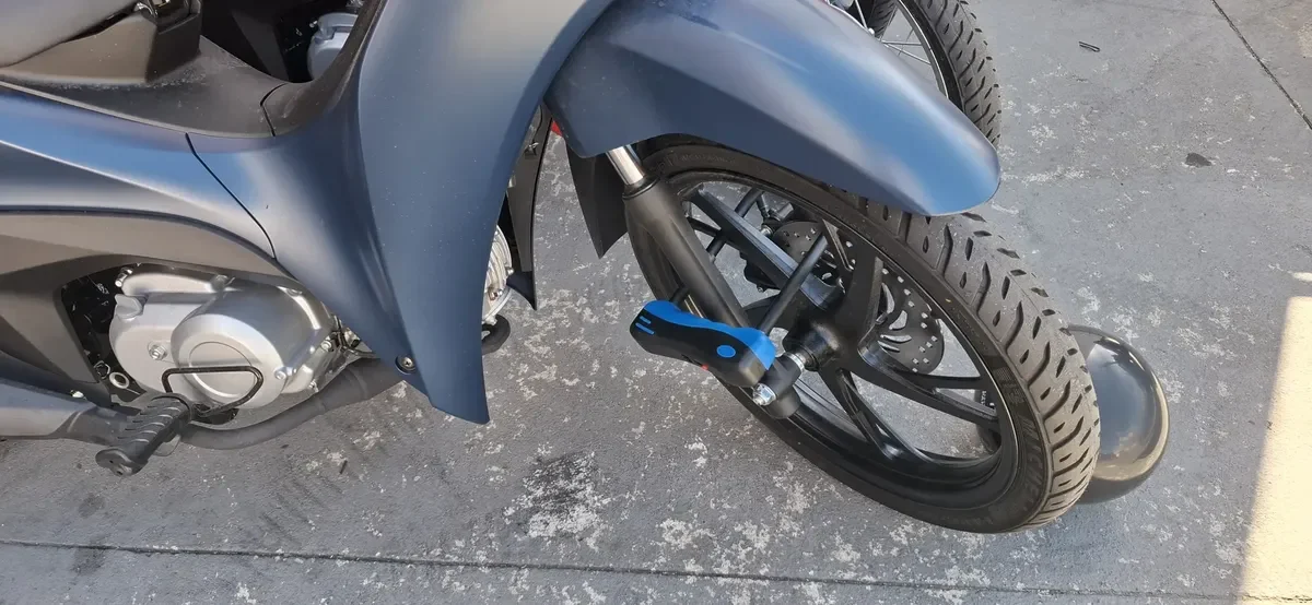 Cadeado em U azul travando a roda dianteira de uma moto azul, passando entre os raios e o garfo, um dos acessórios para scooter elétrica de segurança
