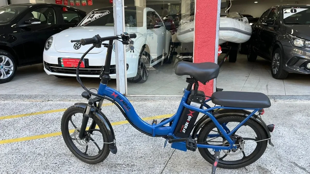 Shineray E-bike azul de lado, com banco duplo e roda traseira com freio a disco, em frente a uma loja de veículos